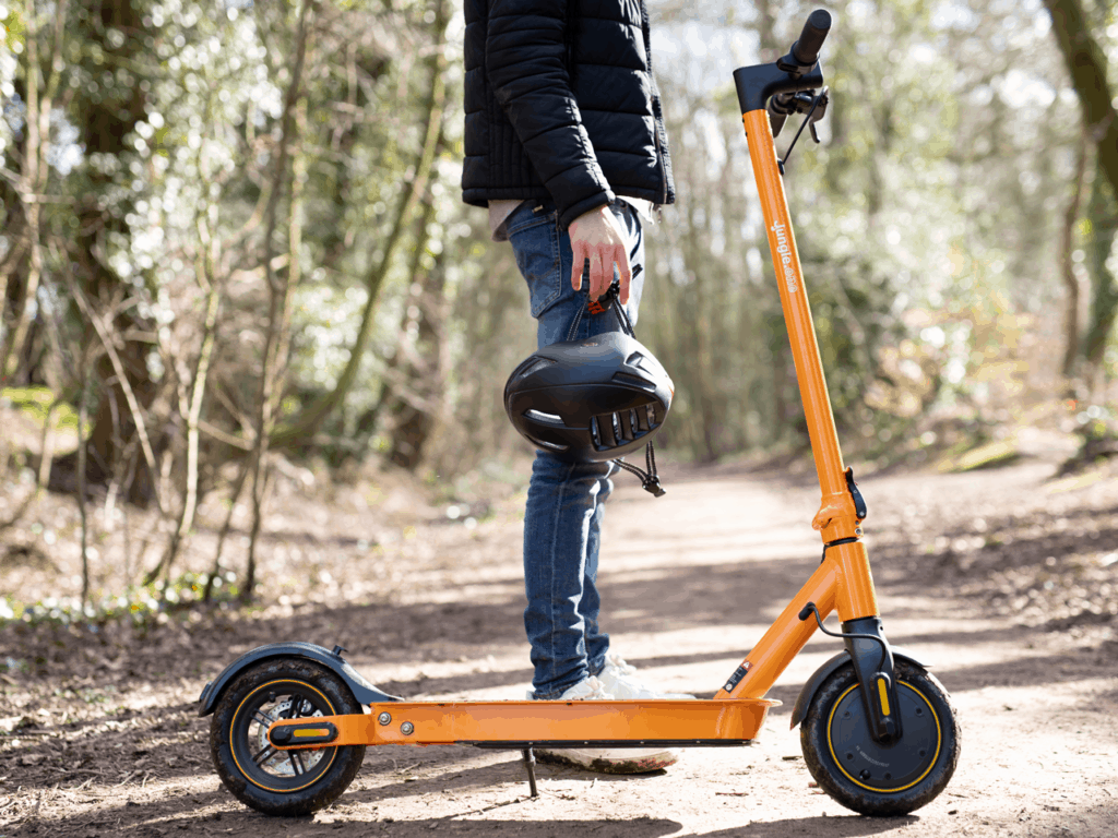 man holding helmet with orange electric scooter in forest